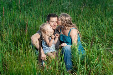 Obraz premium Mother and daughter kissing daddy outdoors. Happy family.