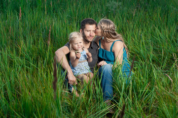 Fototapeta premium Happy family. Mother and daughter kissing daddy outdoors