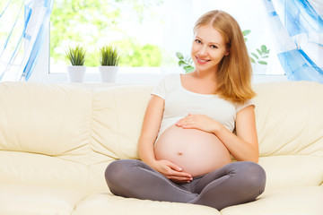 happy pregnant woman is resting at home on sofa