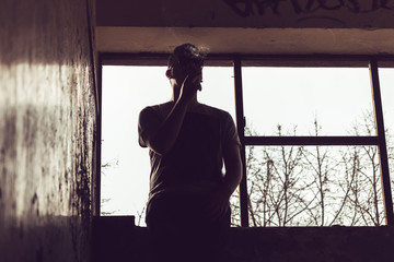 Sillouette of a man sitting on a window ledge smoking a cigarette