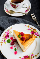 Cheesecake slice with raspberries and mint leaves on plate.