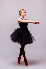 Young blonde ballerina girl dance and posing in black tutu and ballet shoes on grey background. Siries of photo. Ballerina concept.