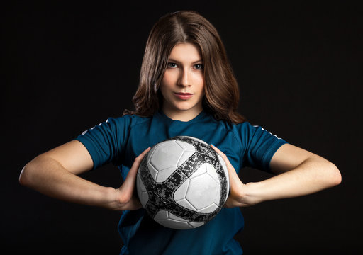 young female soccer player standing and holding the ball