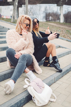 Outdoor lifestyle portrait of two best friends, smiling and having fun together, enjoy each other company posing and making selfie pictures to each other and share happiness
