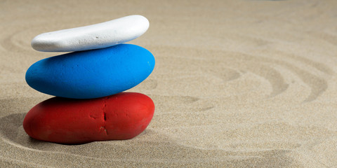 Fototapeta na wymiar Une pile de galet en équilibre sur le sable , couleur rouge, bleu, blanc, comme plusieurs drapeaux, format panoramique