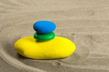 Fototapeta na wymiar Trois galets aux couleurs du brésil, empilés sur le sable