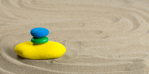 Fototapeta na wymiar Trois galets aux couleurs du brésil, empilés sur le sable, format panoramique