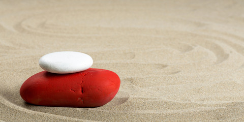 Deux galets rouge et blanc sur du sable en format panoramique