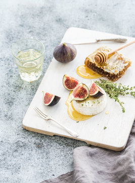 Camembert or brie cheese with fresh figs, honeycomb and glass of white wine on serving board over grunge rustic grey backdrop