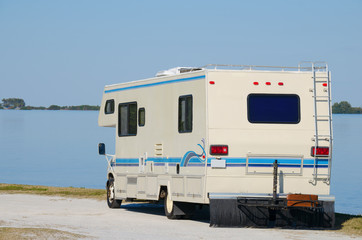 A RV recreational vehicle parked by edge of water at beautiful beach on a bright sunny blue sky day