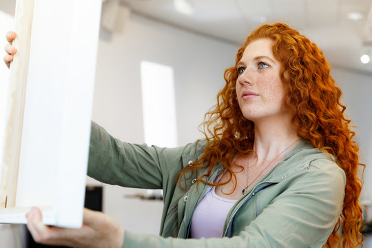 Young caucasian woman standing in art gallery front of  paintings