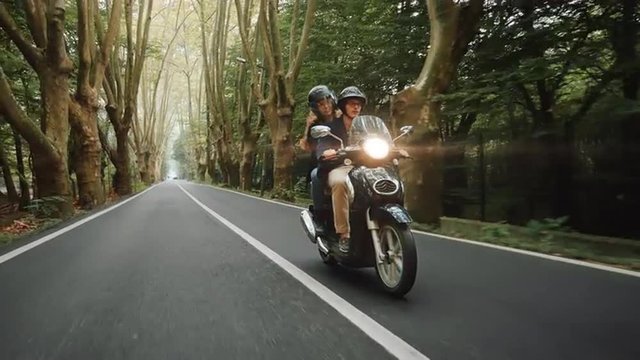 Young Caucasian heterosexual couple rides their scooter on country road