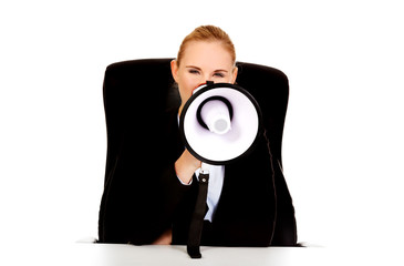 Business woman sitting behind the desk and screaming through a megaphone