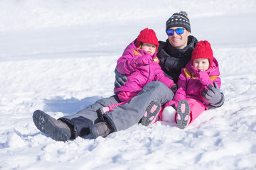 Fototapeta na wymiar Happy father sitting in snow with his two daughters