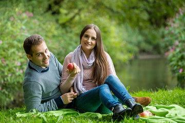 Young beautiful couple having picnic on the lawn in summer park. Woman and man  happy smile looking at the camera.