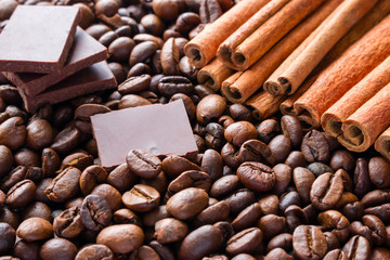 slices of dark chocolate on the background of cinnamon sticks and coffee beans