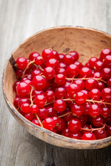 Redcurrant on a branch close to a wooden bowl.