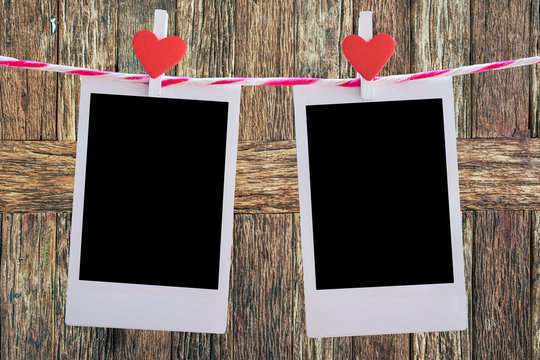 2 Blank instant photo and red clip paper heart hanging on the clothesline with old wood background.Designer concept.