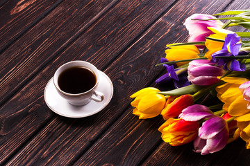 Fototapeta na wymiar Cup of coffee and bouquet of tulips on a wooden background