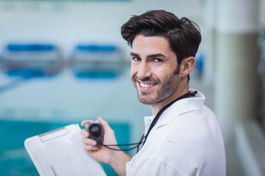 Handsome trainer holding stopwatch and reading clipboard