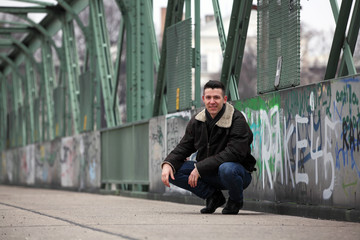 Attractive young man wearing leather jacket squatting on the street