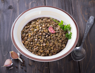 Boiled lentils in a bowl with garlic and black pepper on a wooden table