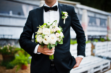Wedding bouquet at hand of groom with bow tie