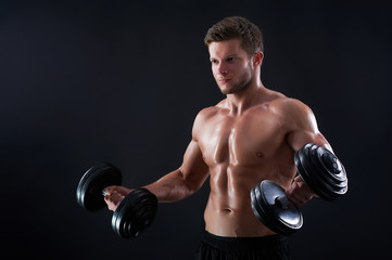 Fototapeta na wymiar Pulling thorough. Portrait of a handsome young fitness man exercising with dumbbells against black background