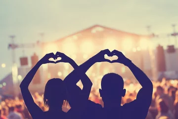 Gartenposter Couple enjoying the concert together while holding a heart-shape symbol with their hands. © astrosystem