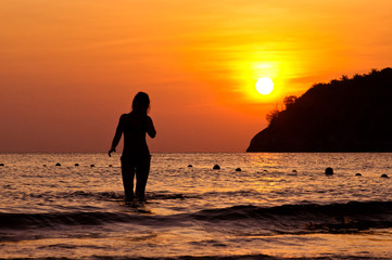 Young woman walking out of Andaman sea on sunset in Phuket island, Thailand