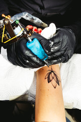 Tattoo artist on black gloves draws with his tattoo machine a lotus flower on client's arm