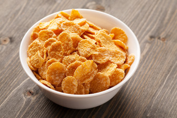Cornflakes in white bowl on gray wooden table