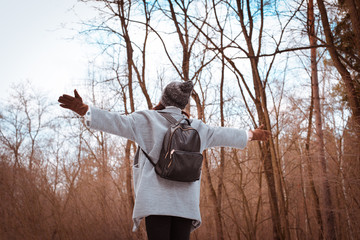 Portrait of a happy beautiful girl with brown hair in  winter forest.Attractive brunette woman dressed in a hipster style with black stylish leather backpack wearing grey coat and white pullover.