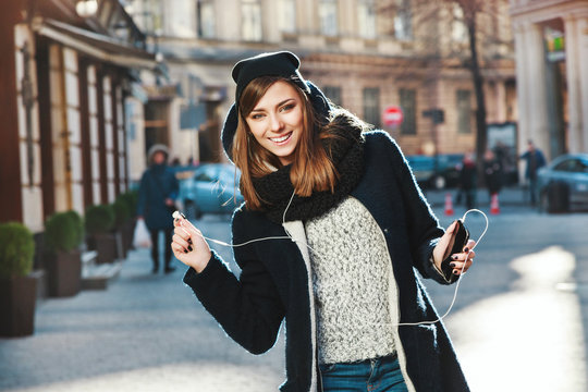 Lovely girl with brown hair wearing headphones on the street