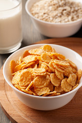 Cornflakes and oatmeal in white bowls on wooden board