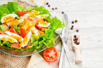
healthy salad with fresh vegetables , tomatoes , lettuce , boiled egg and spices and oil on a wooden background