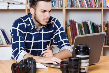 Attractive man wearing blue plaid shirt sitting with laptop