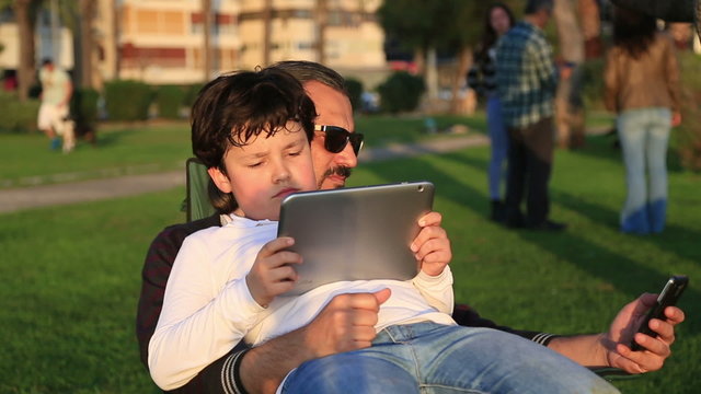 Father and son using smartphone and tablet device each one separately. Social network concept.