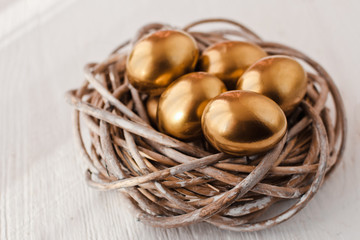 Golden easter eggs in nest on white wooden background