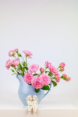 Pink flowers in blue jug. Roses in jug. Two angels.