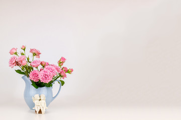 Pink flowers in blue jug. Roses in jug. Two angels on wooden banch.