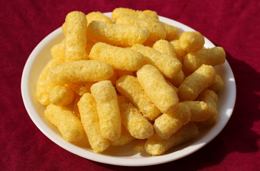 Crunchy corn puffs a tasty snacks in white pate on a red background