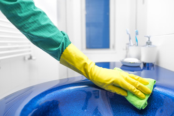 Hand in yellow glove washes sink.