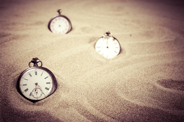 Trois montres à gousset réparties dans le sable d'une plage avec un filtre vintage