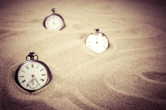 Trois montres à gousset réparties dans le sable d'une plage avec un filtre vintage