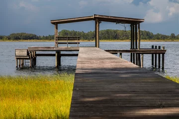 Printed kitchen splashbacks Pier Wooden pier above grass leading to empty boathouse shelter structure with bench on water river lake intracoastal waterway looking peaceful serene tranquil 