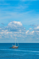 Fototapeta premium Isolated sailboat on blue ocean sea with white fluffy clouds in clear blue sky looking restful relaxing calm isolated secluded private