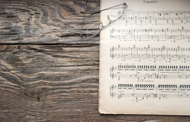 Naklejka premium Altes, vergilbtes Notenblatt für Piano mit Brille, Holz / Treibholz Hintergrund
