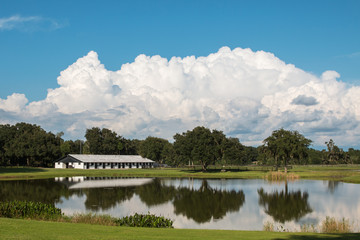 White equine horse barn on farm ranch with reflection in water pond lake and blue sky and white...