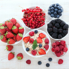 Berries, strawberries, raspberries, currants, blackberries, blueberries, nuts, milk and muesli  ingredients for healthy breakfast  on white wooden table.